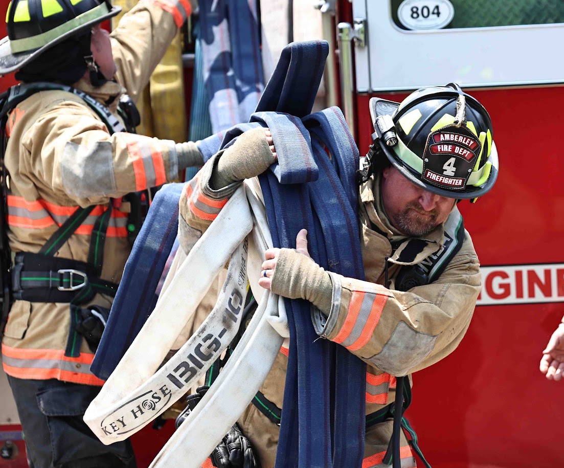 Firefighter carrying hose from truck to unseen destination while second firefighter unravels hosing from the pumper
